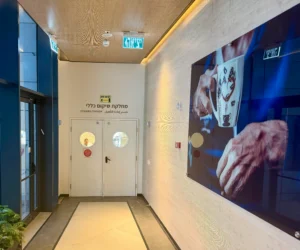 מסדרון עם דלתות כפולות שעליהן כתוב "שיקום" בעברית ובאנגלית; על הקיר הימני תלויה תמונה גדולה של ידיים אוחזות בספל קפה.