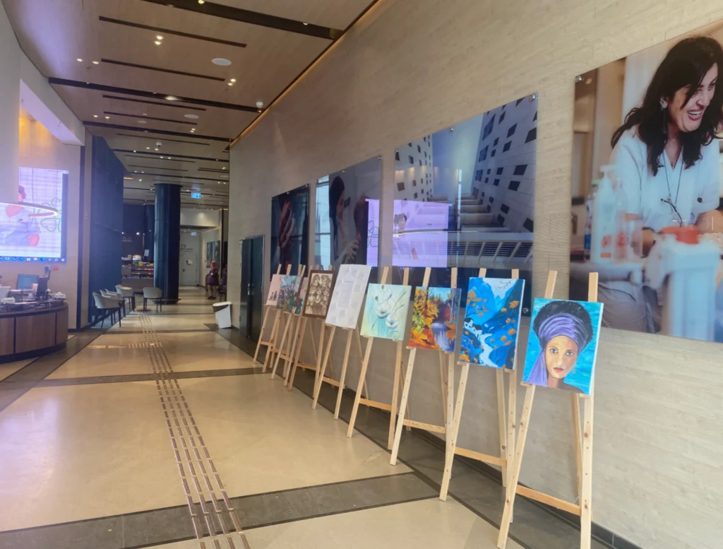 ציורים על כן מוצגים במסדרון מודרני עם דיוקנאות ויצירות אמנות מופשטות, לצד תמונות קיר גדולות ופינות ישיבה הנראות ברקע.