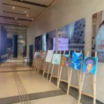 ציורים על כן מוצגים במסדרון מודרני עם דיוקנאות ויצירות אמנות מופשטות, לצד תמונות קיר גדולות ופינות ישיבה הנראות ברקע.